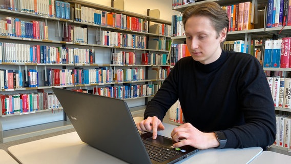 Ein junger Mann sitzt vor einer Bücherwand an einem Tisch vor seinem Laptop. © NDR Foto: Johannes Tran