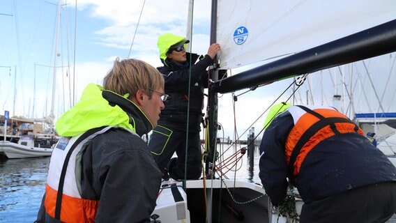 Leon und Alexander Tyssen arbeiten mit einer weiteren Person am Hafen auf einem Segelboot. © NDR Foto: Marina Heller