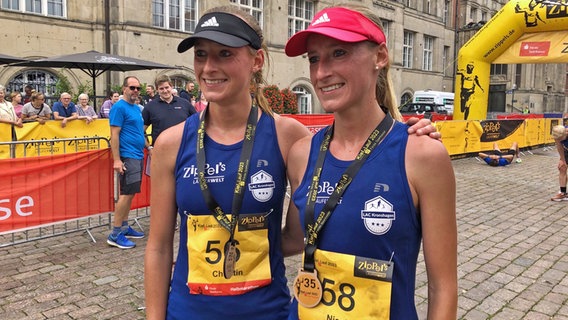 Zwei ähnlich aussehende Läuferinnen stehen für ein Foto nach Zieleinlauf beim KielLauf 2023 auf dem Kieler Rathausplatz. © NDR Foto: Rudolf Dautwiz