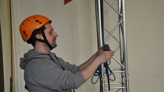 Ein Mann mit Sicherheitshelm bindet ein Seil an ein Klettergerüst.  Foto: Peter Bartelt