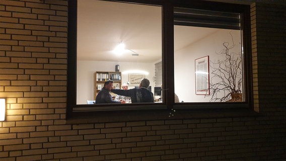 Ein Blick durch ein Fenster: Innen sitzen vier Männer an einem Tisch und unterhalten sich. © NDR Foto: Johannes Tran