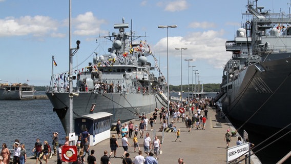 Menschen laufen auf der Kieler Woche zwischen Marineschiffen. © picture alliance / rtn - radio tele nord | rtn, ute strait Foto: Ute Strait