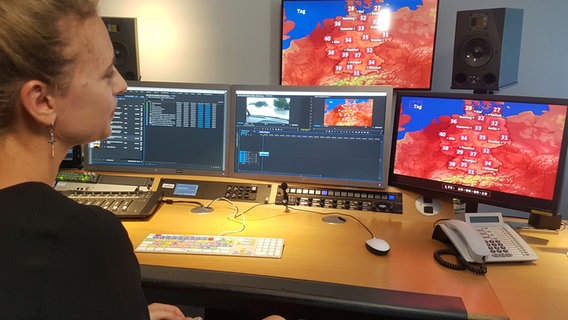 Friederike Otto sitzt in einem Büro vor vielen Monitoren, auf denen eine Wetterkarte von Deutschland zu sehen ist. Die meisten Bereiche sind rötlich eingefärbt. © NDR Foto: Cassandra Arden