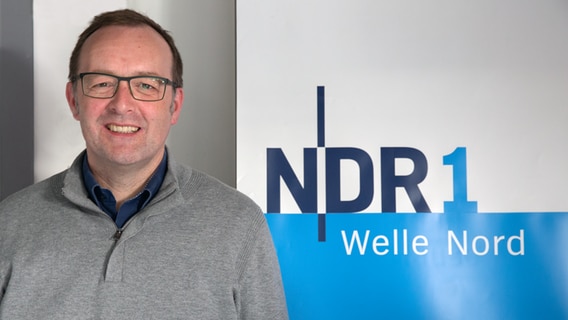 Prof. Dr. Wilhelm Knelangen lächelt neben einem NDR1 Welle Nord Aufsteller in die Kamera. © NDR Foto: Christoph Klipp