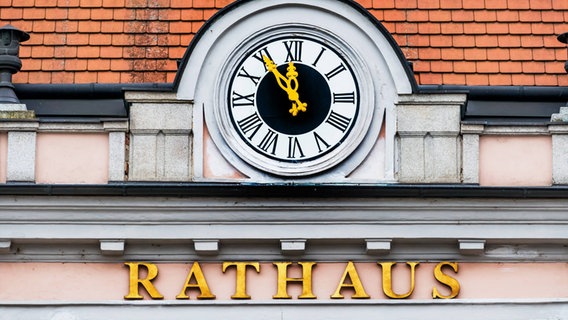 Eine Uhr an einem Dachgiebel steht auf fünf vor zwölf und darunter steht mit goldenen Buchstaben "Rathaus". © Imago Images / McPHOTO Foto: McPHOTO