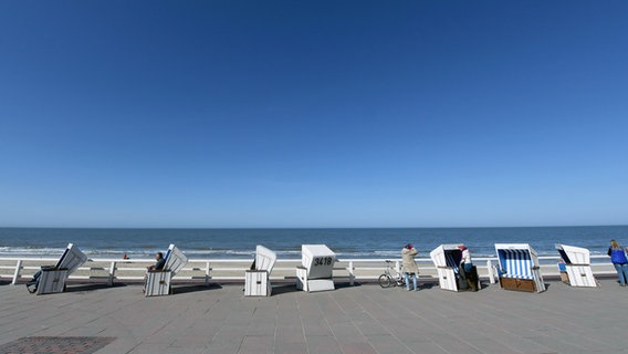 An der Strandpromenade von Westerland auf Sylt stehen zahlreiche leere Strandkörbe unter strahlend blauem Himmel. © dpa Foto: Carsten Rehder