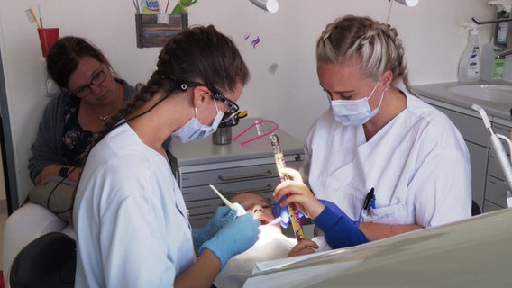 Ein Mädchen hält einen bunten Stab in der Hand, während sie beim Zahnarzt behandelt wird. © NDR 
