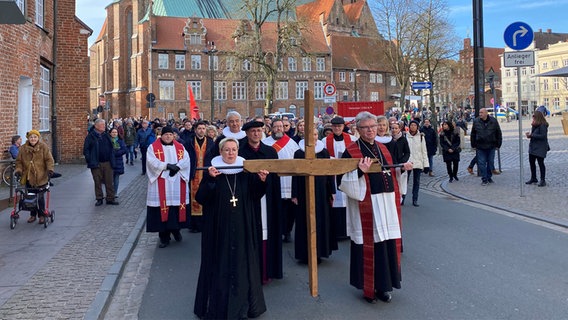 Beim Lübecker Kreuzweg tragen Geistliche ein Kreuz vor sich und werden dabei von zahlreichen Menschen begleitet. © NDR Foto: Linda Ebener