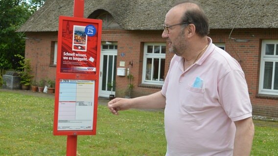 Peter Kroll, der Bürgermeister von Alveslohe, schut auf einen Busfahrplan. © NDR Foto: Anne Passow