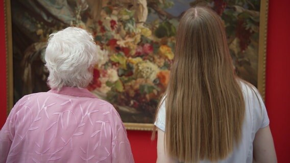 Eine Seniorin und eine junge Frau stehen vor einem Gemälde. © NDR 