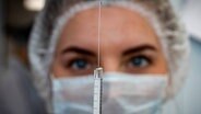 Eine Frau hält eine Spritze vor die Augen und sieht auf den Tropfen, der sich aus der Nadel drückt. © imago images / ITAR-TASS Foto: ITAR-TASS