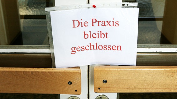 An einer Tür zu einer Arztpraxis hängt ein Schild mit der Aufschrift "Die Praxis bleibt geschlossen". © dpa bildfunk Foto: Patrick Pleul
