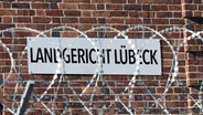 Ein Schild mit der Aufschrift "Landgericht Lübeck" hängt an der Außenwand hinter Stracheldraht. © Christophe Gateau/dpa Foto: Christophe Gateau