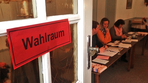 Ein roter Zettel mit der Überschrift Wahlraun hängt an einer Tür. Im Raum sind Menschen am Schreibtisch zu sehen © NDR Foto: Jörg Jacobsen