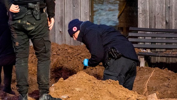Zwei Einsatzkräfte stehen am Rand eines Lochs. Eine weitere Person rechts steht gebückt und richtet eine Taschenlampe in die Grube. © dpa-Bildfunk Foto: Daniel Bockwoldt