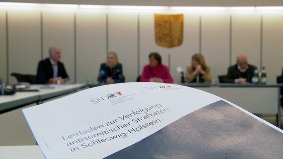 Ein Heft mit dem Schriftzug "Leitfaden zur Verfolgung antisemitischer Straftaten in Schleswig-Holstein" legt auf einem Tisch bei einer Pressekonferenz © NDR 