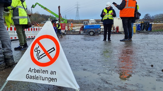 Ein Warnschild mit dem Schriftzug "Arbeiten an Gasleitungen" steht auf dem Boden an einer Baustelle. © NDR Foto: Oliver Kring