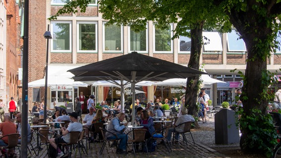 Several people are sitting under umbrellas in a square in Lübeck.  © NDR Photo: Finja sulfur