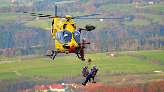 Rettungskräfte hängen angeseilt an einem Hubschrauber.  