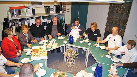 Alle Mitarbeiter sitzen an einem runden Tisch und frühstücken © NDR Foto: Thorsten Philipps