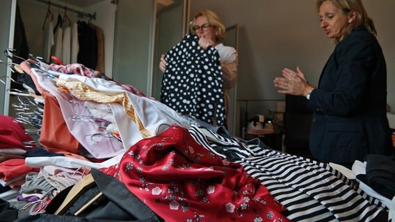 Patricia Knötzsch (rechts) sieht Astrid Saalmann beim Aussortieren von Kleidern zu, auf dem Bett vor ihnen liegt ein großer Stapel Klamotten. © NDR Foto: Jennifer Lange