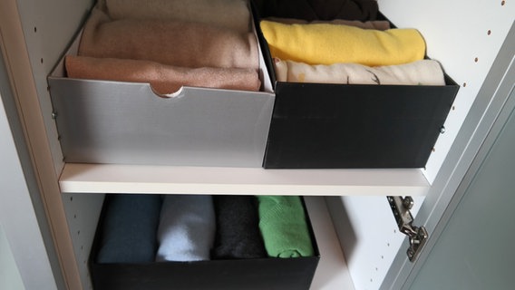 Ordentlich mit gefalteten Pullovern gefüllte Schuhkartons stehen in einem Schrank. © NDR Foto: Jennifer Lange