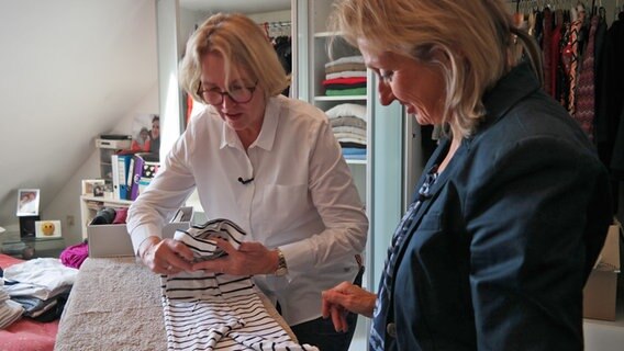 Patricia Knötzsch (rechts) beobachtet, wie ihre Kundin Astrid Saalmann einen Pullover auf einem Bügelbrett faltet. © NDR Foto: Jennifer Lange