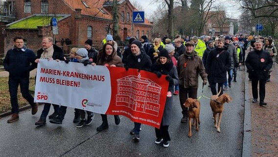Demonstranten tragen in Lübeck ein Banner vor sich mit der Aufschrift: "Marien-Krankenhaus muss bleiben". © NDR Foto: Julian Marxen