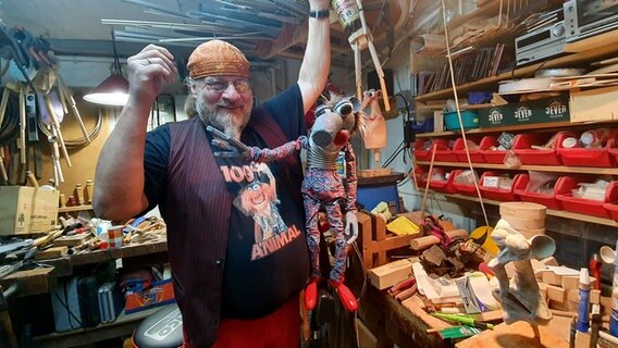 Der Marionettenbauer Peter Bayer steht in seiner Werkstatt und hält eine Marionette in die Höhe. © NDR Foto: Sebastian Parzanny