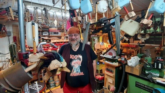 Der Marionettenbauer Peter Bayer steht in seiner vollen Werkstatt und hält eine Marionette in den Händen. © NDR Foto: Sebastian Parzanny