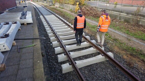 Zwei Bauarbeiter laufen über die Gleisen einer Bahnerneuerung. © NDR 