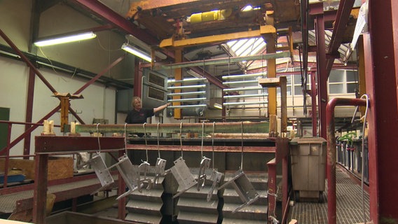 Ein/ Eine Mitarbeiter*inn neben einer großen Maschine zur Metallverarbeitung. © NDR 