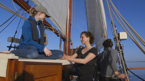 Emma Hilgenstock (links) sitzt an Deck des Traditionsseglers Albin Köbis und spricht mit Lauren Grüterich (rechts) Emma Hilgenstock (links) sitzt an Deck des Traditionsseglers Albin Köbis und spricht mit Lauren Grüterich (rechts) © NDR Foto: Johanna Jannsen
