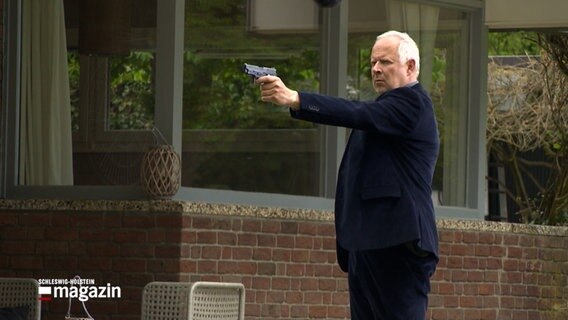 Tatort-Schauspieler Axel Milberg hält eine Pistole in der Hand. © NDR 
