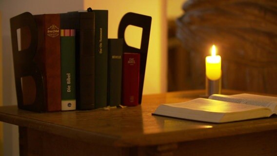 Mehrere Bibeln und Gesangsbücher stehen bei Kerzenschein in einer Kirche. © NDR Foto: NDR
