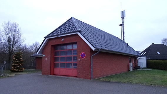 An einem neueren Feuerwehrgerätehaus ist hinten ein Mast mit einer Mobilfunkantenne befestigt. © NDR Foto: Peer-Axel Kroeske