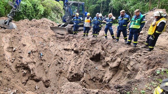 Mehrere Rettungskräfte und ein Bagger stehen an einem Erdloch Mehrere Rettungskräfte und ein Bagger stehen an einem Erdloch © NDR Foto: Cassandra Jane Arden