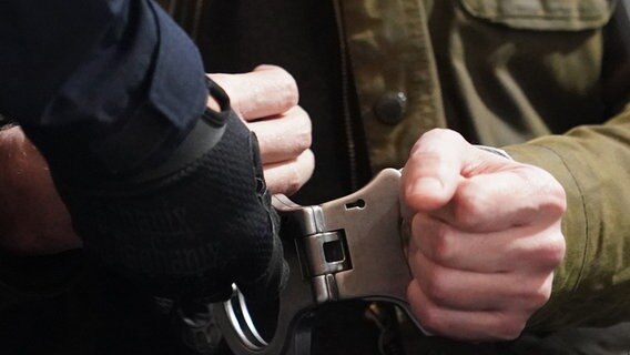 Ein Justizbeamter nimmt dem Angeklagten die Handschellen zu Beginn des Prozesses wegen eines Dreifachmordes im Sitzungssaal des Landgerichts ab. © dpa-Bildfunk Foto: Marcus Brandt/dpa