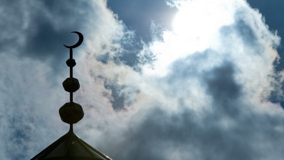 Der Halbmond auf dem Minarett einer Moschee hebt sich als Schattenriss vor Wolken ab. © picture alliance / dpa | Boris Roessler Foto: Boris Roessler