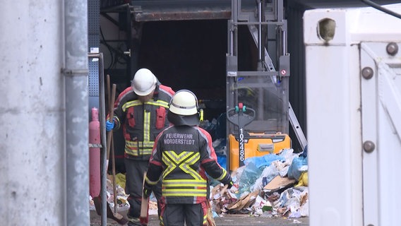 Einsatzkräfte der Feuerwehr arbeiten an einer Müllpresse. © NDR 