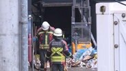 Einsatzkräfte der Feuerwehr arbeiten an einer Müllpresse. © NDR 