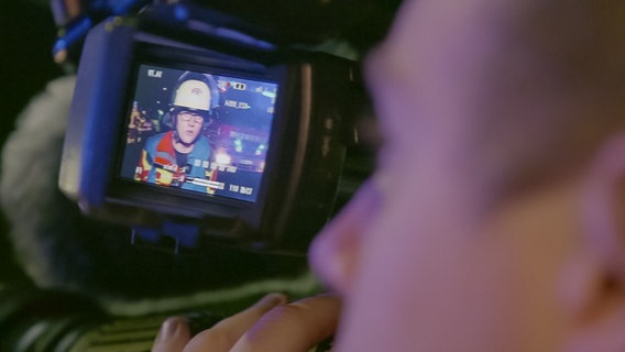 Ein Kameramann hält eine große Fernsehkamera auf seiner Schulter bei einem nächtlichen Einsatz auf einer Straße. Ein Kameramann hält eine große Fernsehkamera auf seiner Schulter bei einem nächtlichen Einsatz auf einer Straße. © NDR