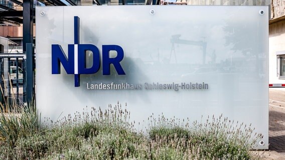 Das NDR-Logo ist an der Einfahrt zum Landesfunkhaus Schleswig-Holstein auf einer Glasplatte angebracht. © dpa Foto: Axel Heimken