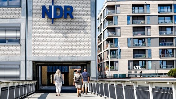 Passanten gehen vor der Einfahrt zum Landesfunkhaus Schleswig-Holstein des NDR entlang. © dpa Foto: Axel Heimken