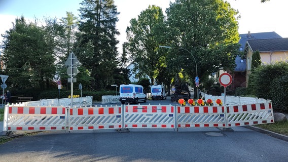 Die Nerongsallee ist auf ganzer Breite mit rot-weißen Barrieren abgesperrt. Dahinter stehen zwei Transporter der Baufirma. © NDR Foto: Peer-Axel Kroeske