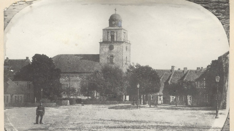 Eine historische Grafik des Kleinflecken in Neumünster. Auf dem Platz vor der Kirche steht ein Mann in Uniform. © Archiv Alfred Heggen