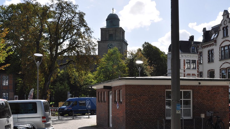 Eine aktuelle Aufnahme des Kleinflecken in Neumünster. Auf dem Platz vor der Kirche stehen viele Autos. © NDR Foto: Anne Passow