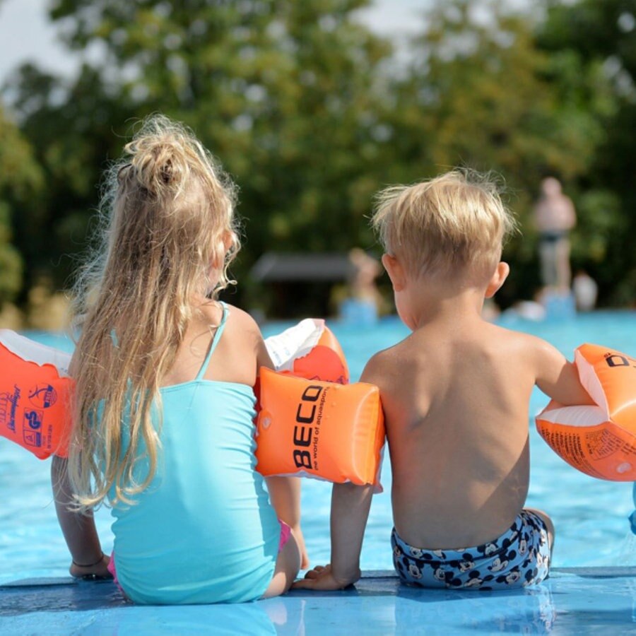 Zwei Kinder sitzen mit Schwimmflügeln am Rand eines Freibads. © dpa-Bildfunk Foto: Frank May