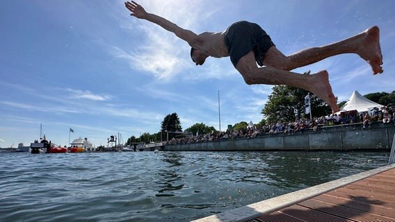 Ein Mann springt, von Zuschauern an der Kiellinie beobachtet, in die Kieler Förde. © NDR Foto: Samir Chawki