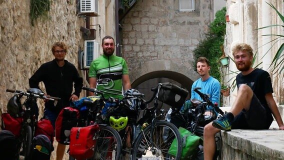 Vier Männer stehen bei ihren Fahrrädern und Gepäck. Sie lächeln in die Kamera.  Foto: Projekt Open Eyes
